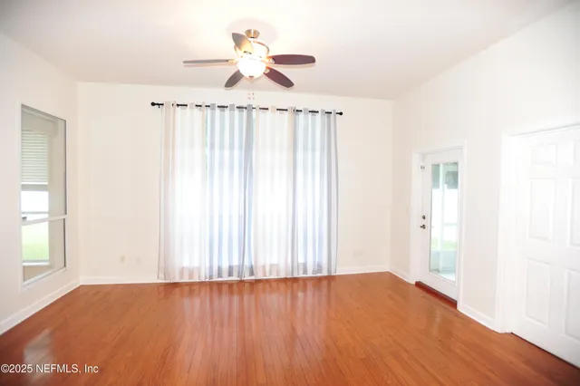 an empty room with wooden floor chandelier fan and windows