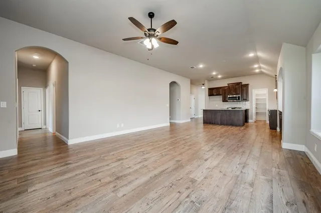a view of an empty room and kitchen with wooden floor