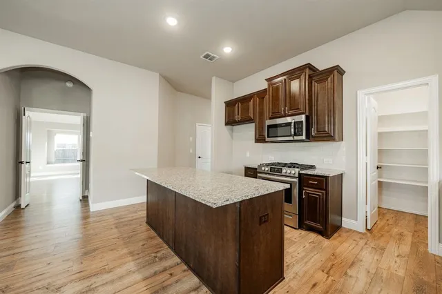 a kitchen with stainless steel appliances granite countertop a stove top oven a sink dishwasher and a refrigerator with wooden floor