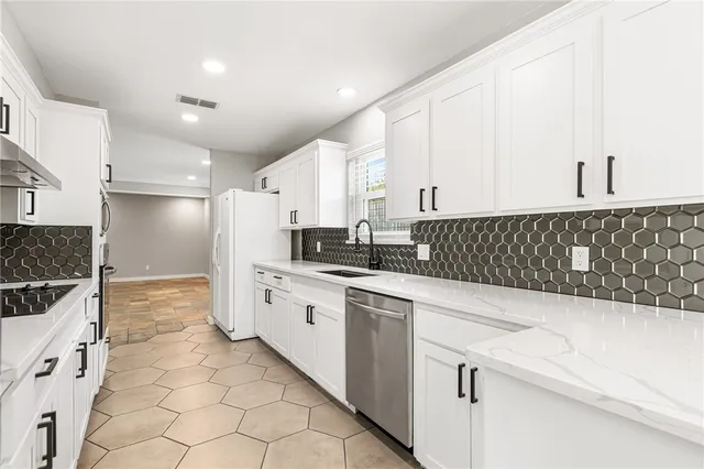 a kitchen with granite countertop a sink a stove a refrigerator and white cabinets