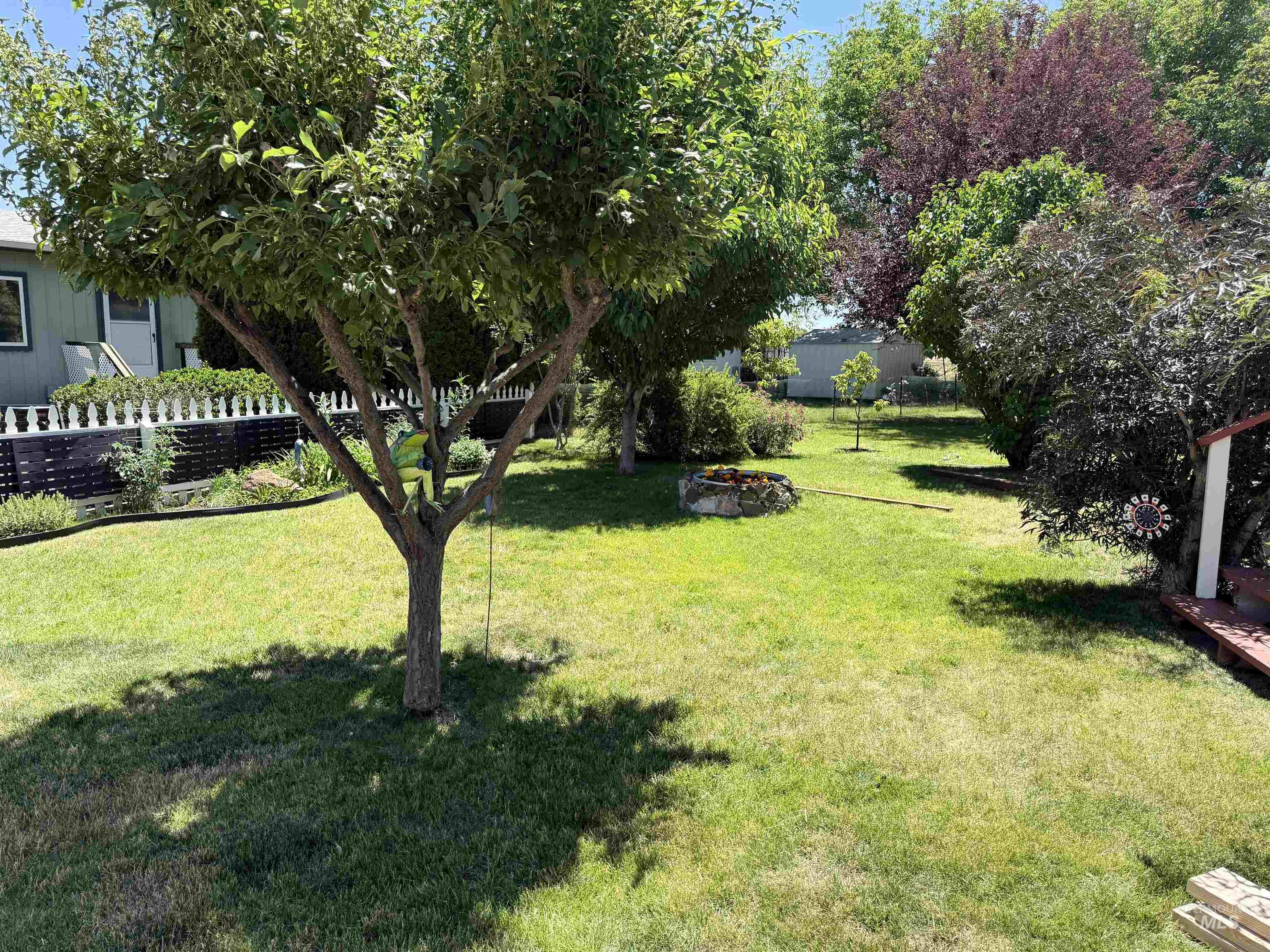2750 Alden Road, Unit 12 12 Fruitland, ID 83619 - Photo 34 of 38 Single-story residence featuring a covered front porch with white railing, a vibrant front garden with various flowering plants, a manicured lawn, and mature trees