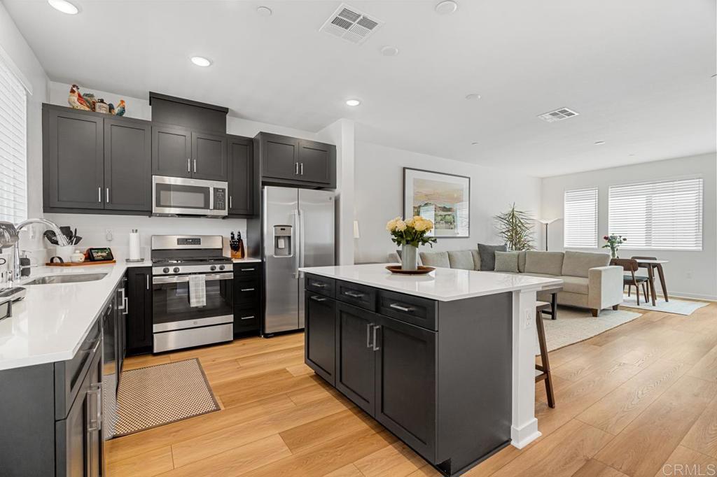 a kitchen with stainless steel appliances granite countertop a stove top oven a sink dishwasher a refrigerator and a dining table with wooden floor