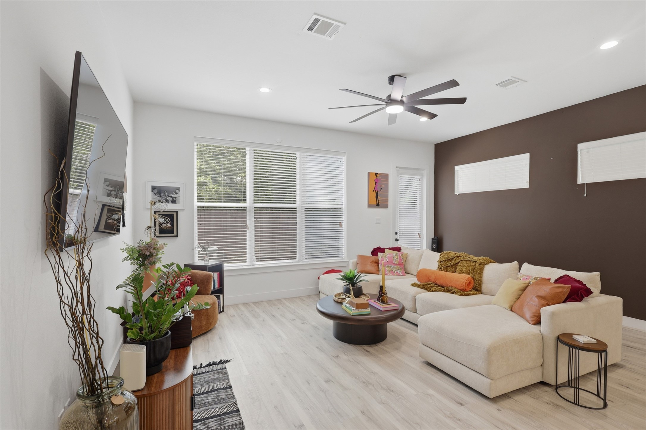 6833 Paris Street Houston, TX 77021 - Photo 4 of 23 Bright, modern living room with large windows, neutral tones, a cozy sectional sofa, and a ceiling fan. Features a wall-mounted TV, stylish decor, and light wood flooring. Ideal for relaxation and entertaining.