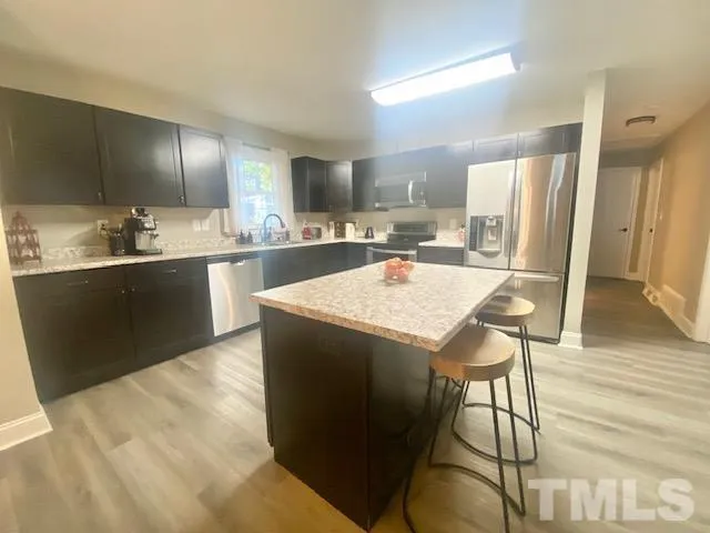 a kitchen with stainless steel appliances granite countertop a sink a stove a refrigerator and a dining table with wooden floor