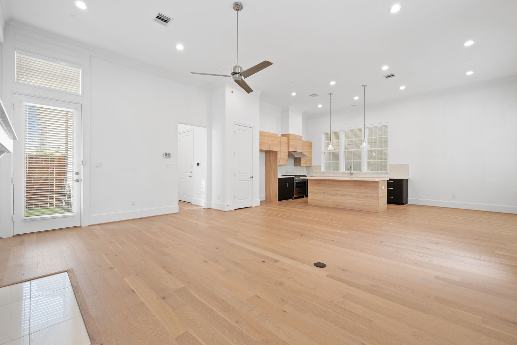 614 Delmar Street Houston, TX 77023 - Photo 5 of 24 This photo showcases a spacious, open-concept living area with light wood flooring, high ceilings, and ample natural light. The modern kitchen features an island with pendant lighting, sleek cabinetry, and stainless steel appliances. A ceiling fan and large windows add to the airy feel.