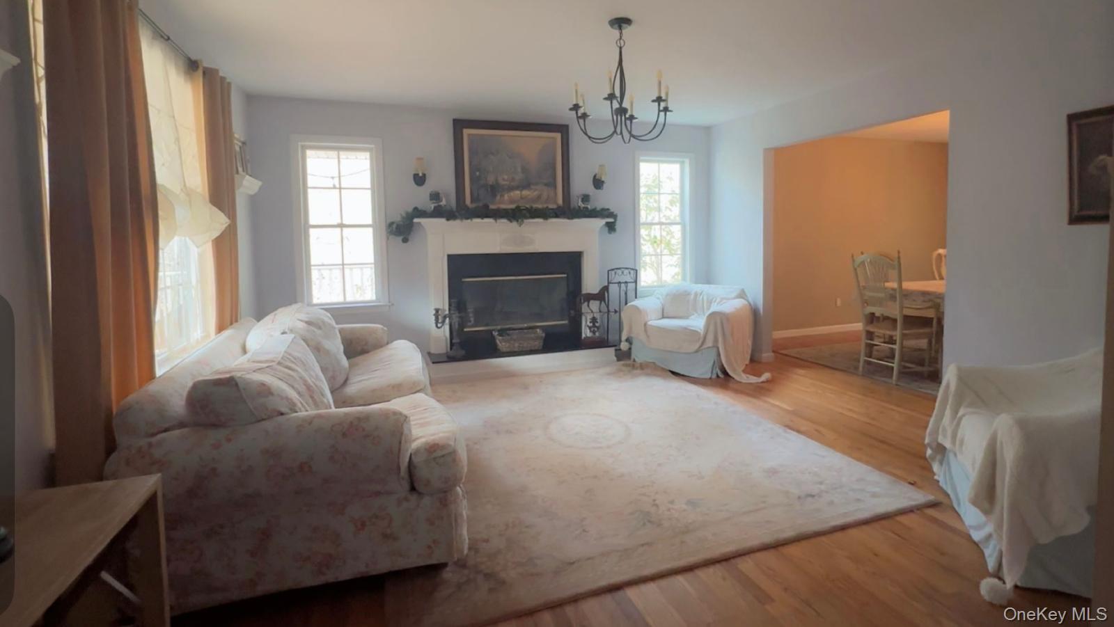 43 North Cozine Road Manorville, NY 11949 - Photo 7 of 42 Living room with light wood finished floors, healthy amount of natural light, a glass covered fireplace, and a chandelier