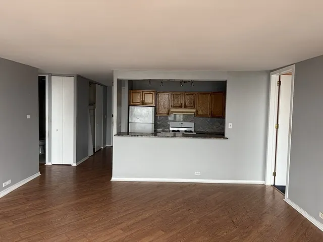 a living room with stainless steel appliances a wooden floor a large window and a kitchen view