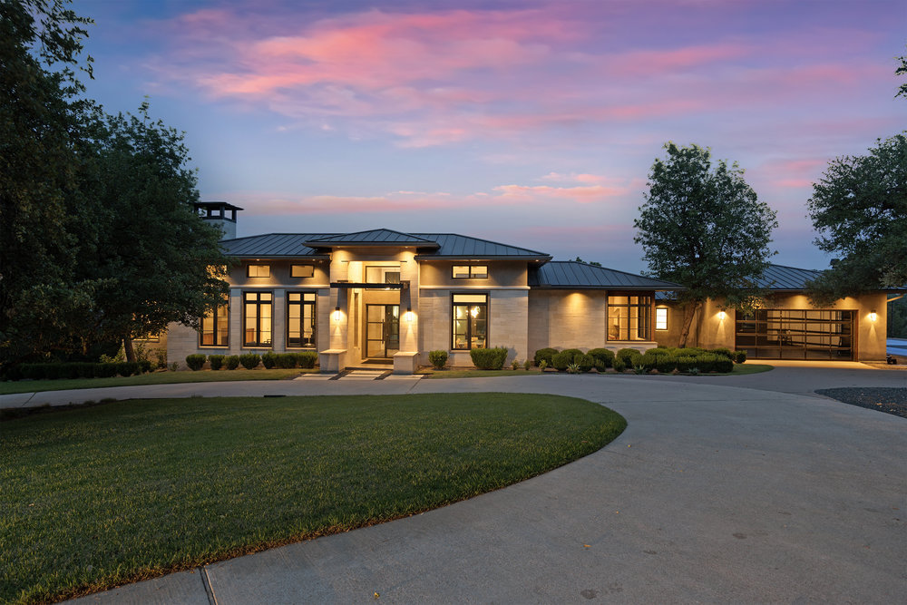 1905 Paisano Road Austin, TX 78746 - Photo 1 of 40 A gracefully curved driveway guides the eye to this striking contemporary residence, illuminated under a vibrant sunset.