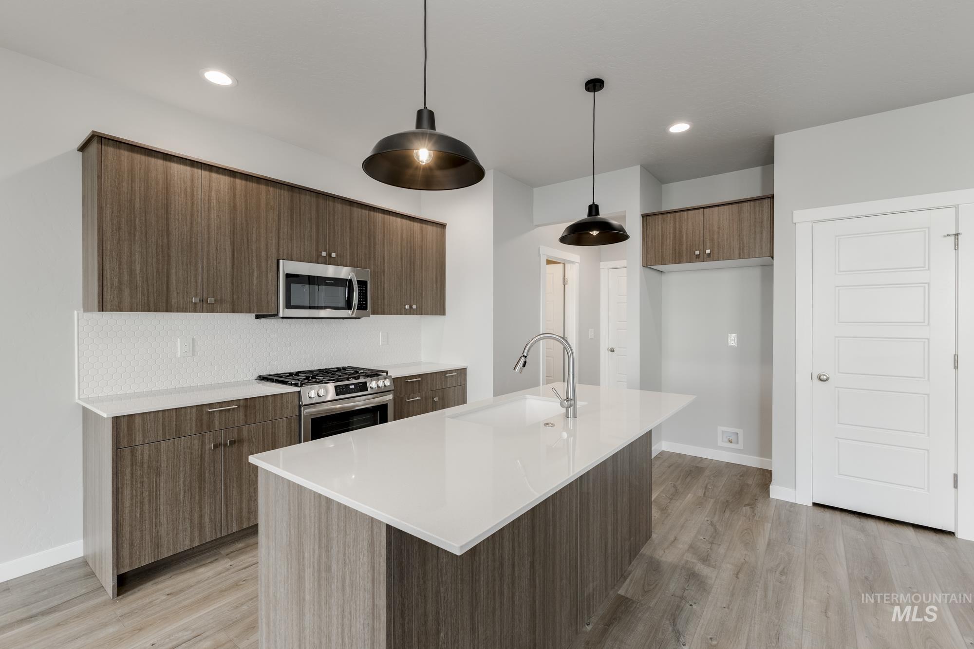 4166 East Kalinga Street Meridian, ID 83642 - Photo 5 of 22 Kitchen with stainless steel appliances, modern cabinets, hanging light fixtures, light stone countertops, and a center island with sink