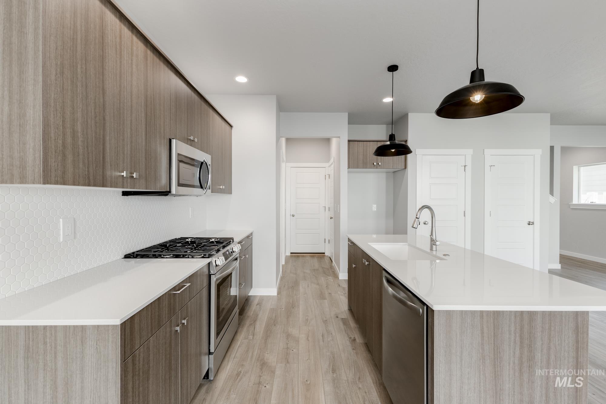 4166 East Kalinga Street Meridian, ID 83642 - Photo 6 of 22 Kitchen featuring appliances with stainless steel finishes, modern cabinets, hanging light fixtures, light wood-style floors, and light stone counters