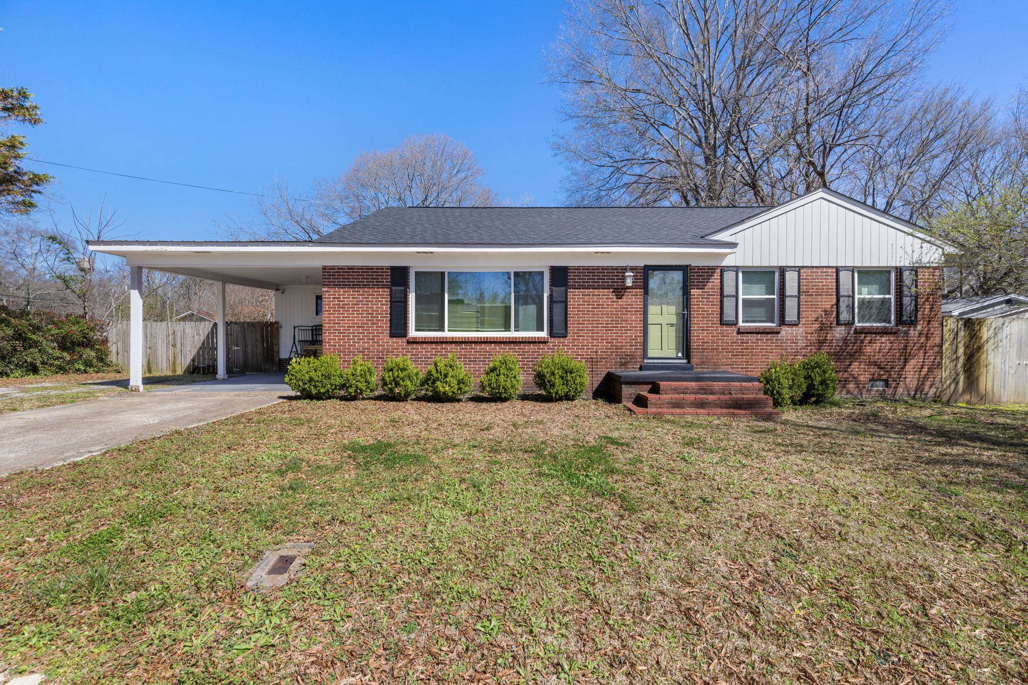 102 West 5th Street Iuka, MS 38852 - Photo 1 of 33 Brick exterior ranch home featuring a covered carport, black framed windows with shutters, a gabled roofline with white siding, and a prominent green front door