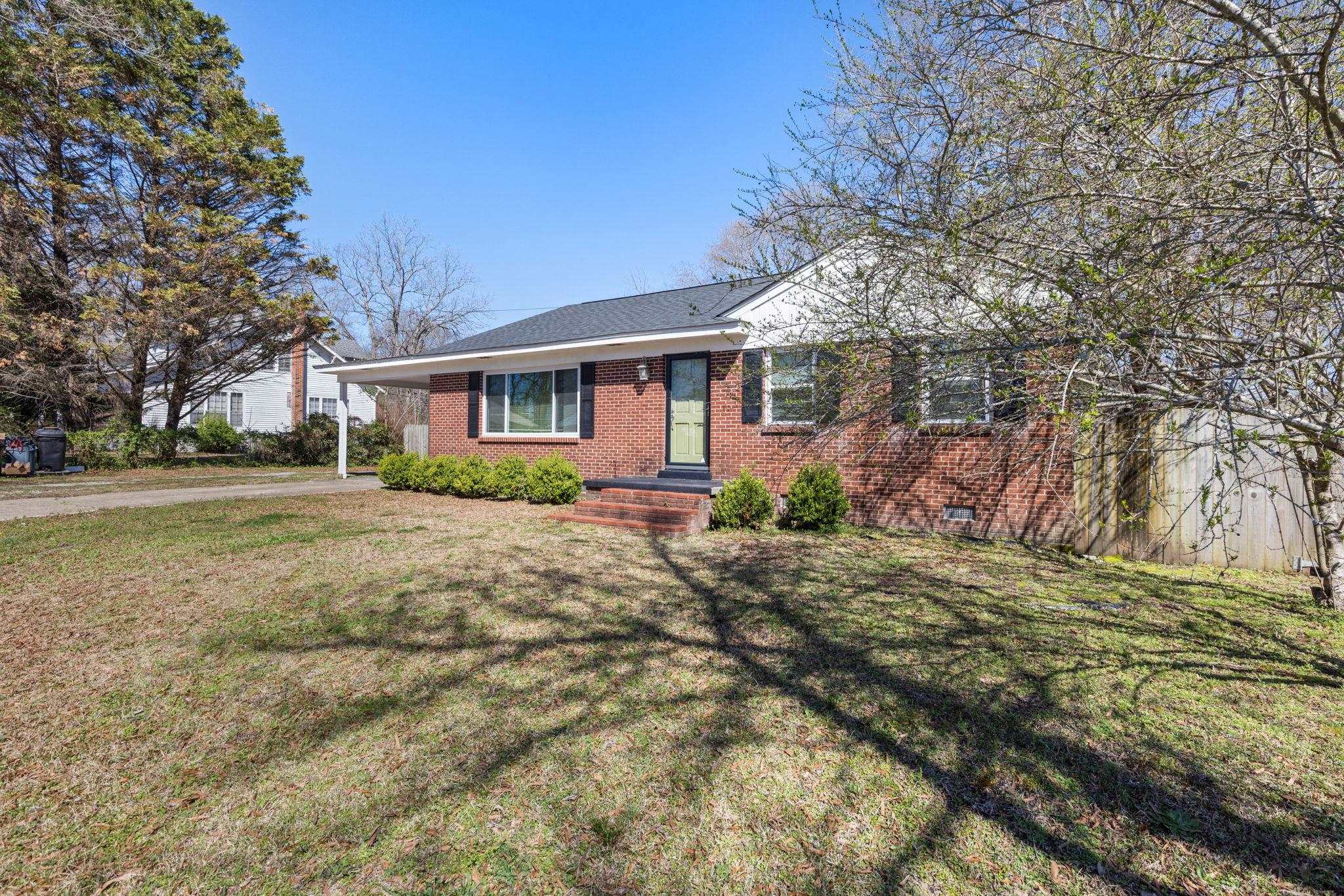 102 West 5th Street Iuka, MS 38852 - Photo 2 of 33 Brick exterior with a dark shingle roof, covered front entry, vibrant green front door, and manicured foundation plantings