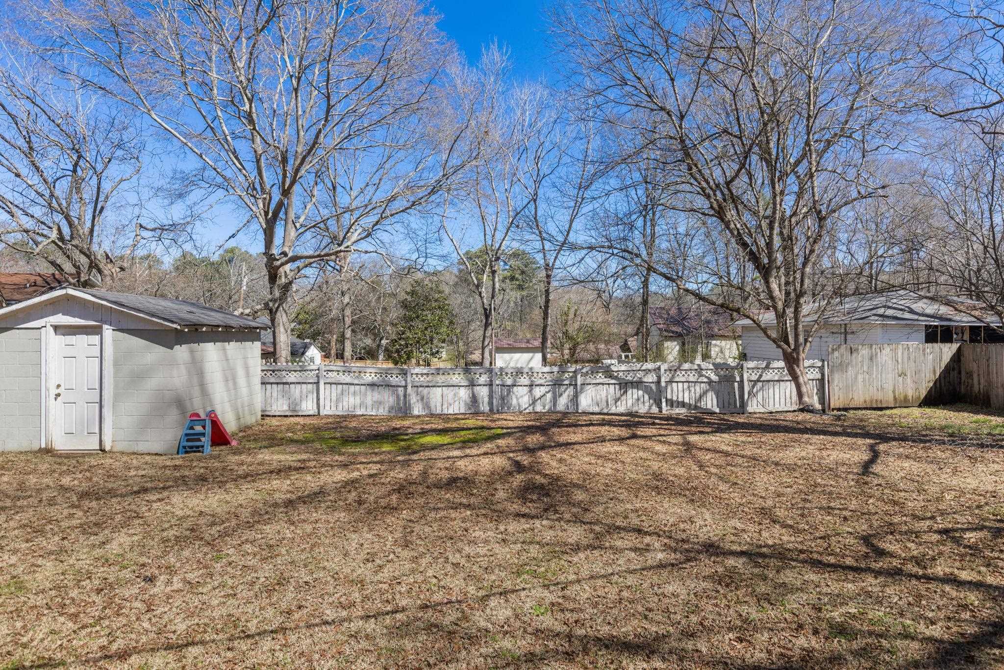 102 West 5th Street Iuka, MS 38852 - Photo 23 of 33 Expansive backyard featuring a white privacy fence, a detached storage building with a single door, and mature deciduous trees