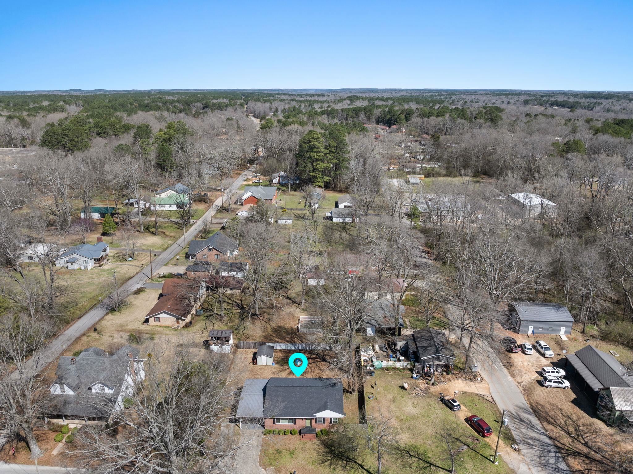 102 West 5th Street Iuka, MS 38852 - Photo 24 of 33 Aerial perspective showcasing a residential property with a dark shingle roof and a brick facade, situated along a paved road
