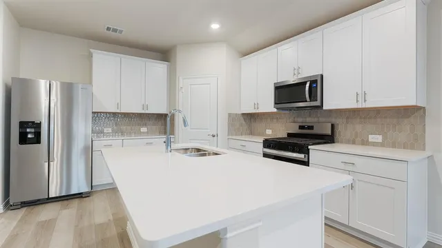 a kitchen with stainless steel appliances a stove a sink a refrigerator white cabinets and a refrigerator