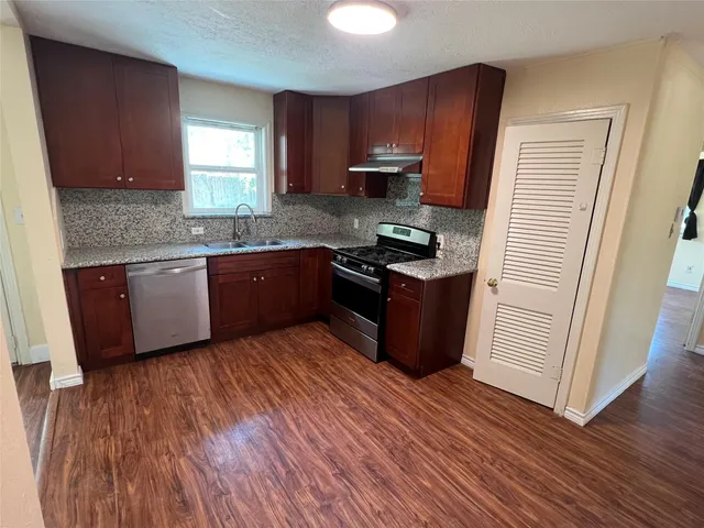 a kitchen with stainless steel appliances granite countertop wooden cabinets a refrigerator a sink a stove a microwave and wooden floors