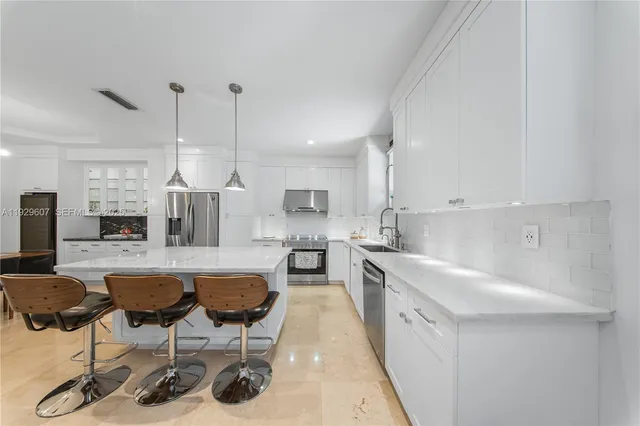 a kitchen with stainless steel appliances kitchen island granite countertop a sink a stove a refrigerator and chairs