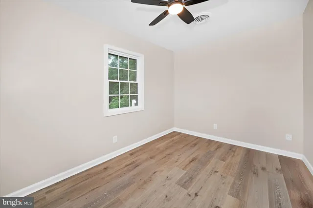 an empty room with wooden floor ceiling fan and window