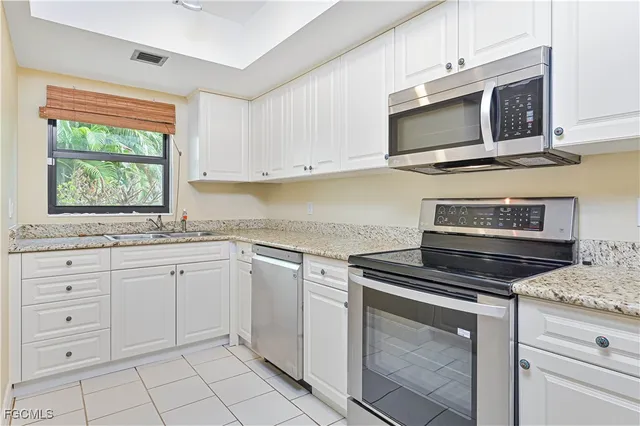 a kitchen with granite countertop white cabinets stainless steel appliances and a window
