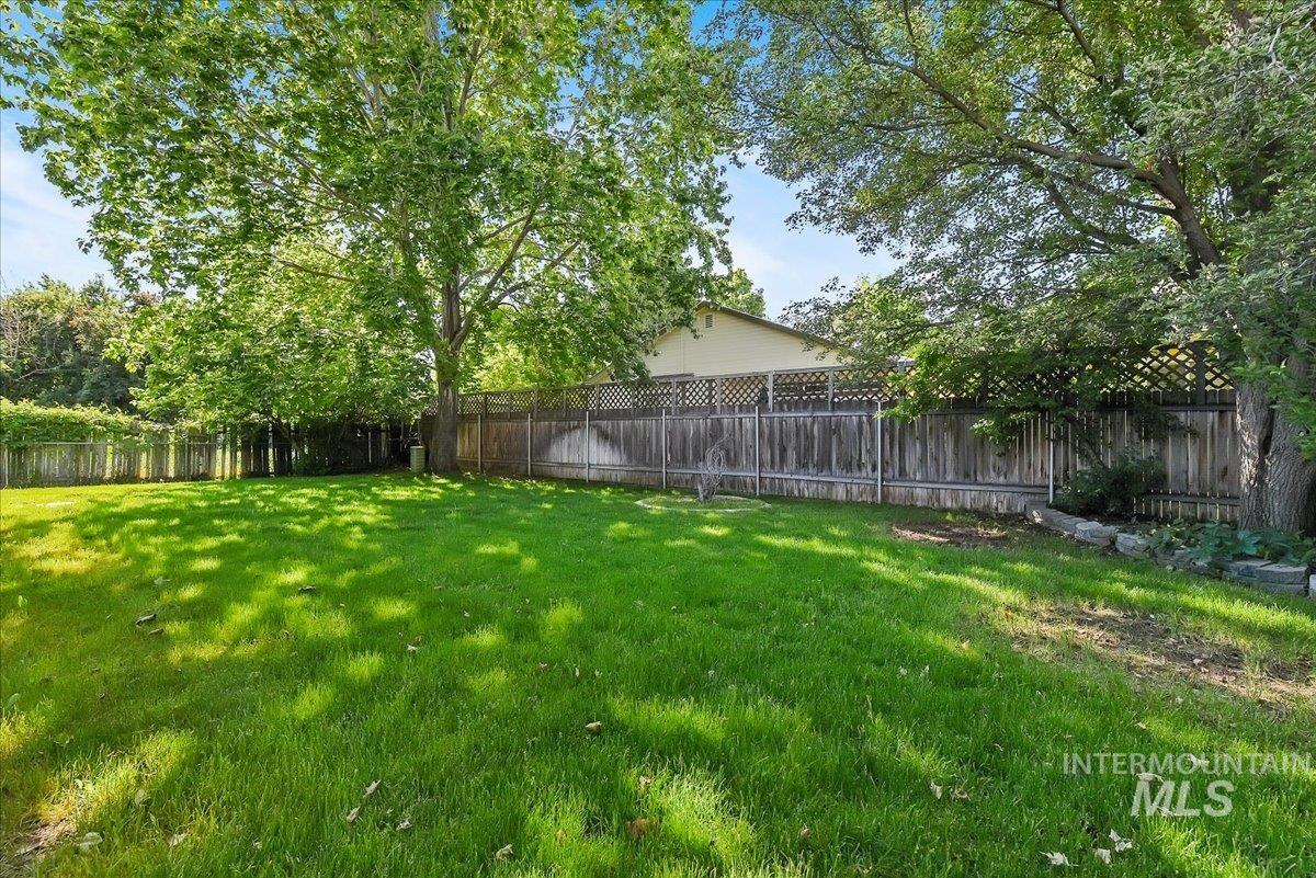 9215 West Preece Street Boise, ID 83704 - Photo 22 of 22 Expansive backyard featuring a lush green lawn, mature trees providing natural shade, and a wood privacy fence
