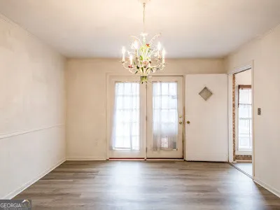 an empty room with wooden floor chandelier and windows