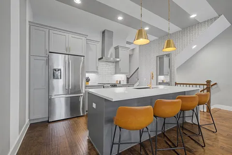 a kitchen with stainless steel appliances granite countertop a sink a stove a refrigerator and a dining table with wooden floor