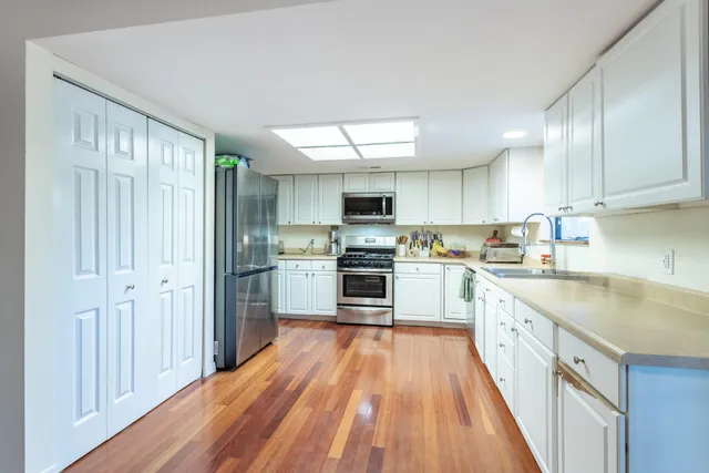 a kitchen with granite countertop a refrigerator oven a sink dishwasher and white cabinets with wooden floor