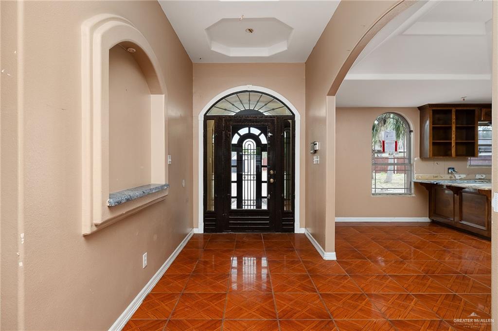 1315 Ruger Street Donna, TX 78537 - Photo 3 of 17 Entryway featuring an arched, dark wood front door with glass panels, geometric tiled flooring, an arched wall niche with a marble-style sill, and an arched doorway leading to an additional space with a window