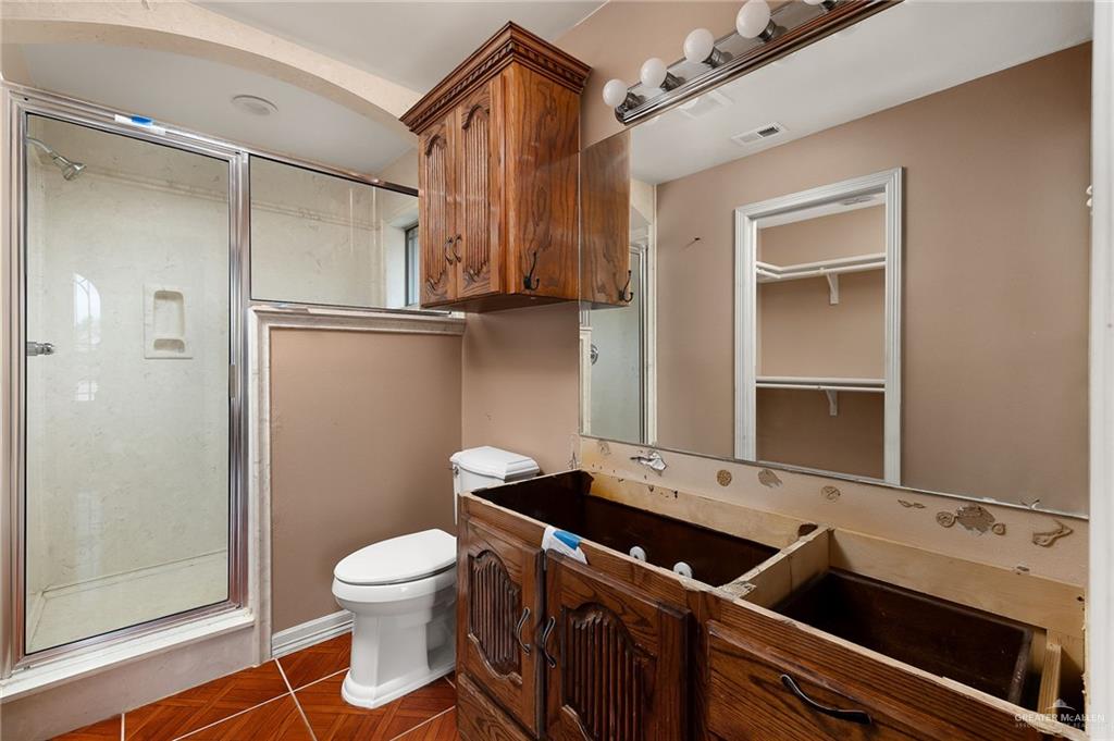 1315 Ruger Street Donna, TX 78537 - Photo 9 of 17 This bathroom features a shower enclosure with a glass door, a white toilet, and a wooden vanity cabinet