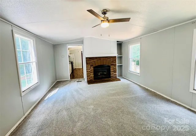an empty room with windows fireplace and a kitchen view