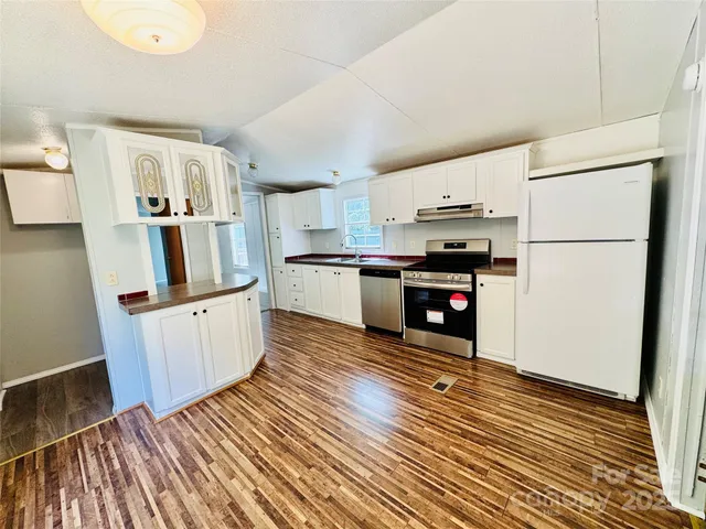 a kitchen with stainless steel appliances granite countertop a refrigerator a stove a sink and white cabinets with wooden floor