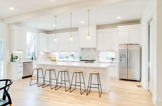 a kitchen with stainless steel appliances kitchen island granite countertop a dining table chairs and white cabinets