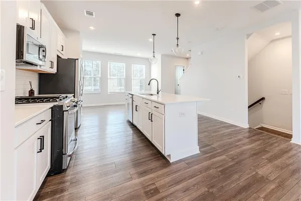 a kitchen with stainless steel appliances a stove top oven a sink a refrigerator white cabinets and wooden floor