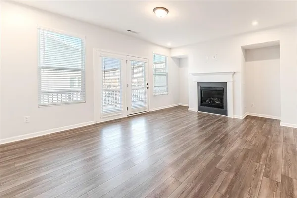 an empty room with wooden floor fireplace and windows