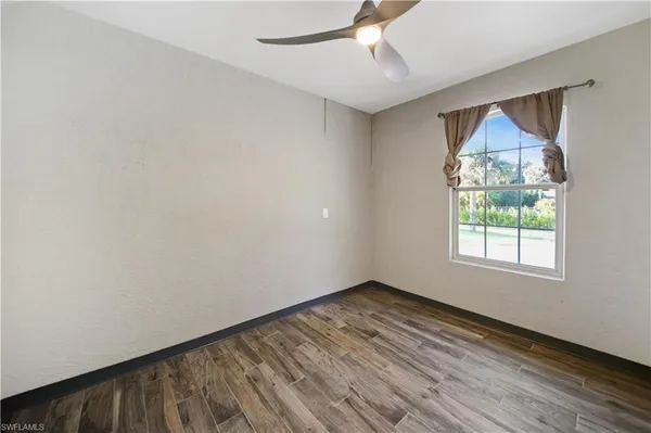 an empty room with wooden floor chandelier fan and windows