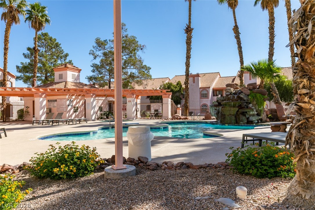 7570 West Flamingo Road, Unit 252 Las Vegas, NV 89147 - Photo 39 of 44 A refreshing pool with an artistic rock waterfall creates a serene oasis amidst palm trees.