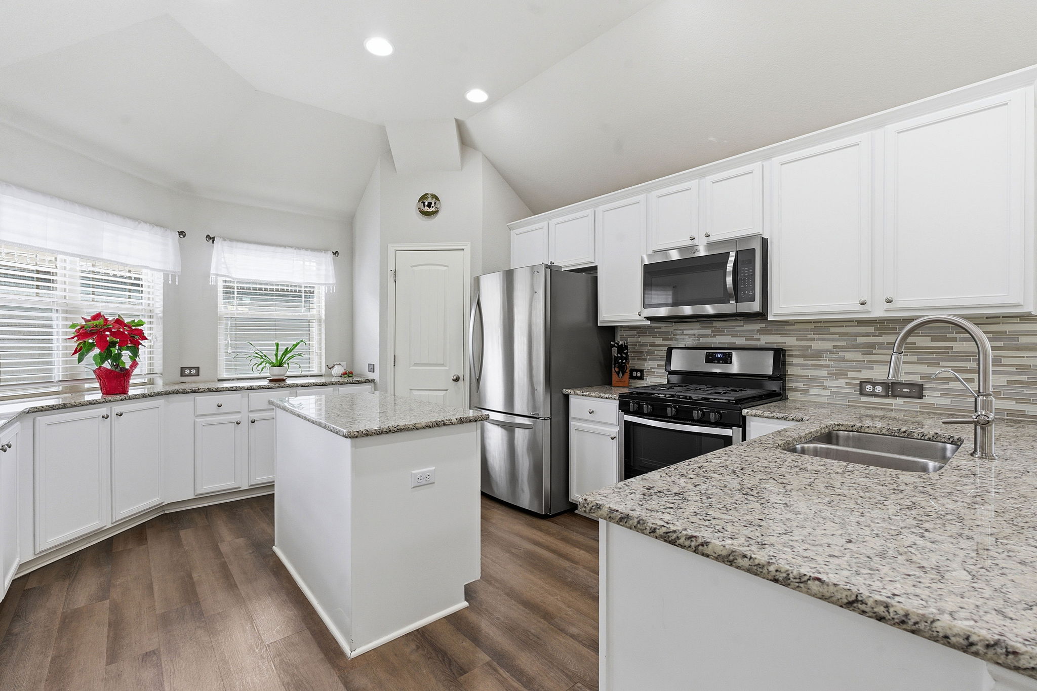 426 Tilly Lane Buda, TX 78610 - Photo 7 of 21 Kitchen with white cabinetry, stainless steel appliances, vaulted ceiling, light stone counters, and a kitchen island