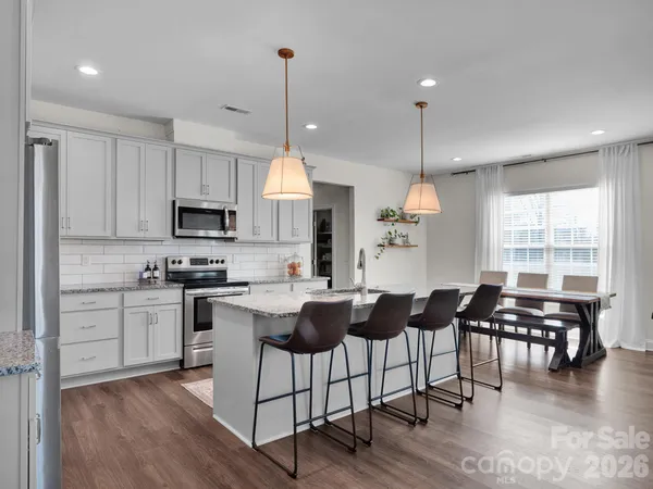 a kitchen with stainless steel appliances kitchen island granite countertop a stove a sink a dining table chairs and view living room