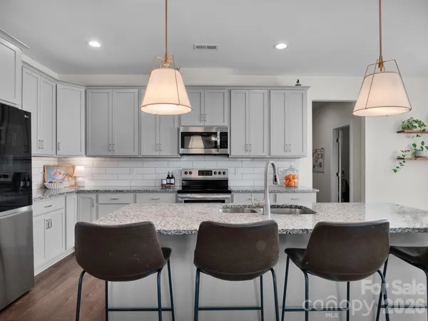 a kitchen with stainless steel appliances granite countertop a stove a sink a microwave a refrigerator and white cabinets