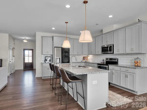 a kitchen with stainless steel appliances granite countertop a stove a sink a microwave a refrigerator and white cabinets with wooden floor