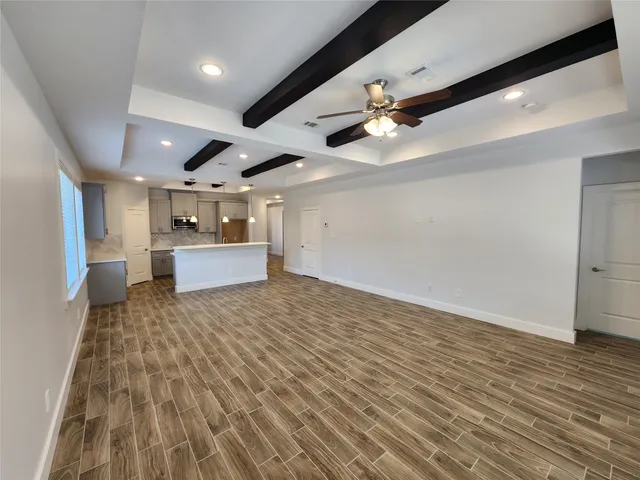 a big room with wooden floor a ceiling fan and kitchen space