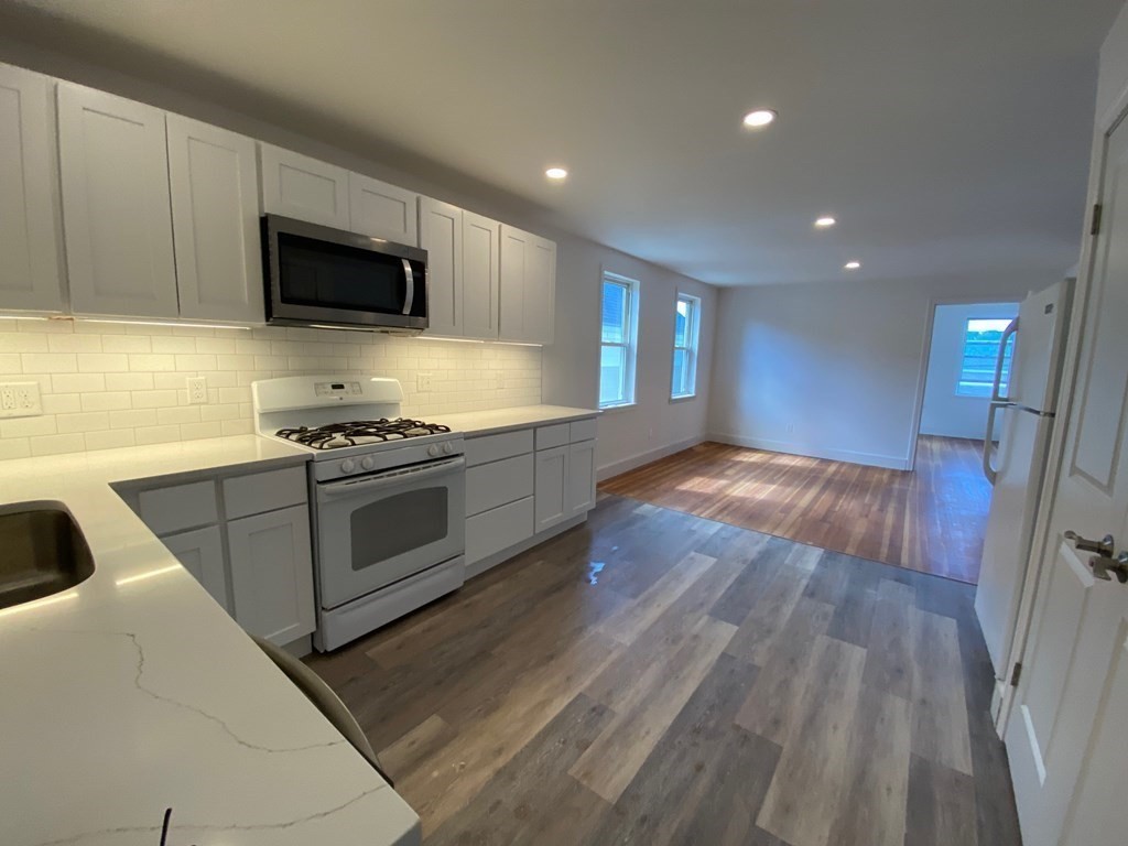 23 Main Street, Unit 2 Topsfield, MA 01983 - Photo 1 of 16 a kitchen with granite countertop wooden floors stainless steel appliances and white cabinets