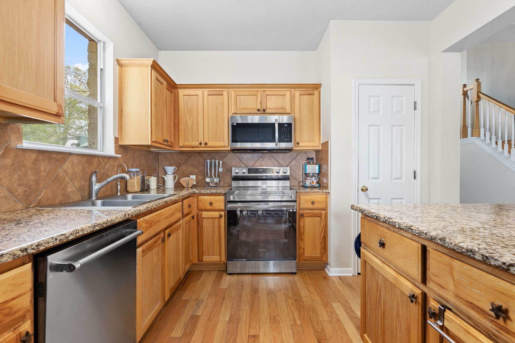 202 The Oaks Boulevard Elgin, TX 78621 - Photo 5 of 40 Kitchen featuring stainless steel appliances, light wood finished floors, light stone counters, and decorative backsplash