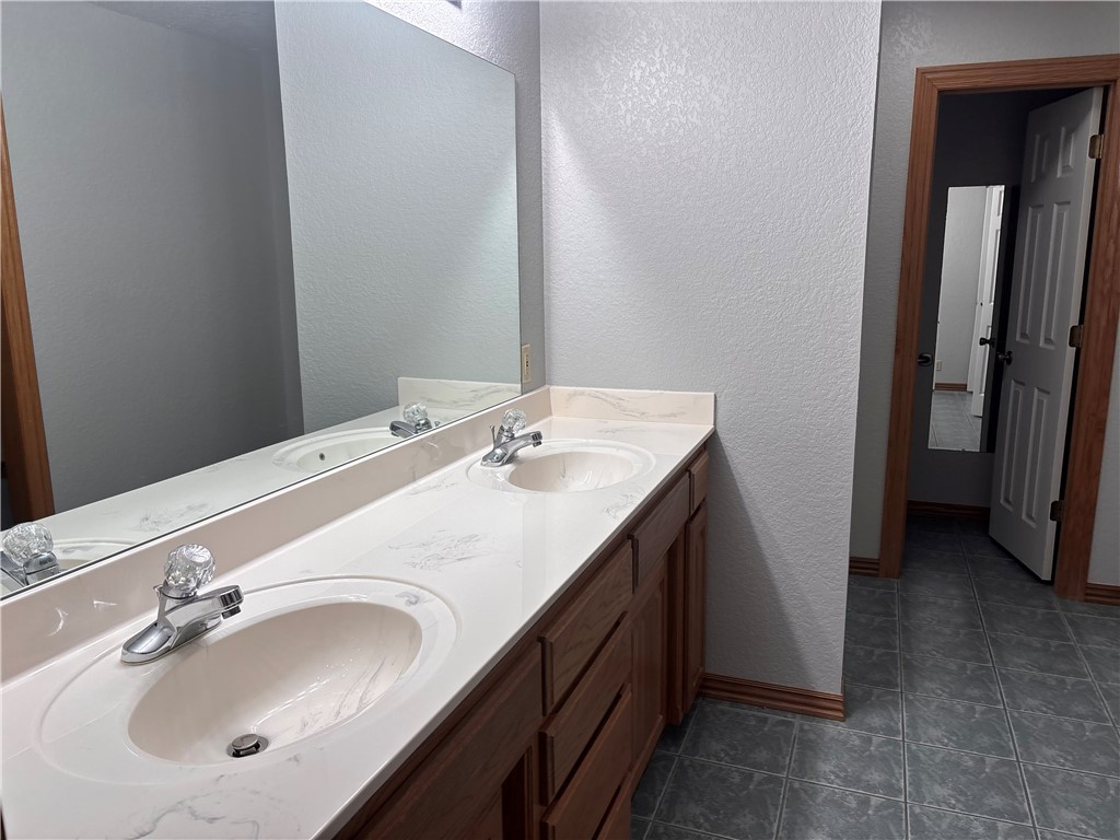 15262 Shipe Road Gravette, AR 72736 - Photo 37 of 60 Double vanity with integrated sinks, expansive wall-mounted mirror, wood-finish cabinetry, and tiled flooring