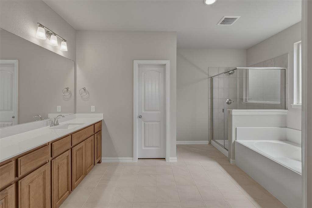 1232 Colca Drive Springtown, TX 76082 - Photo 14 of 23 Bathroom featuring a double vanity with wood cabinetry and white countertops, a large mirror, a separate glass-enclosed shower with tile surround, a built-in tub, and neutral-toned tile flooring