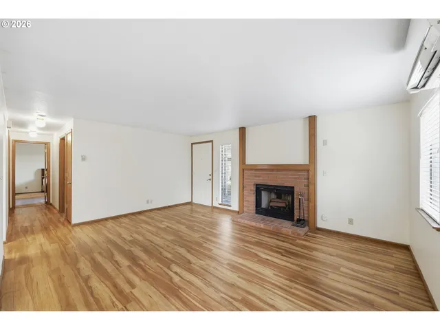 a view of an empty room with wooden floor fireplace and a window