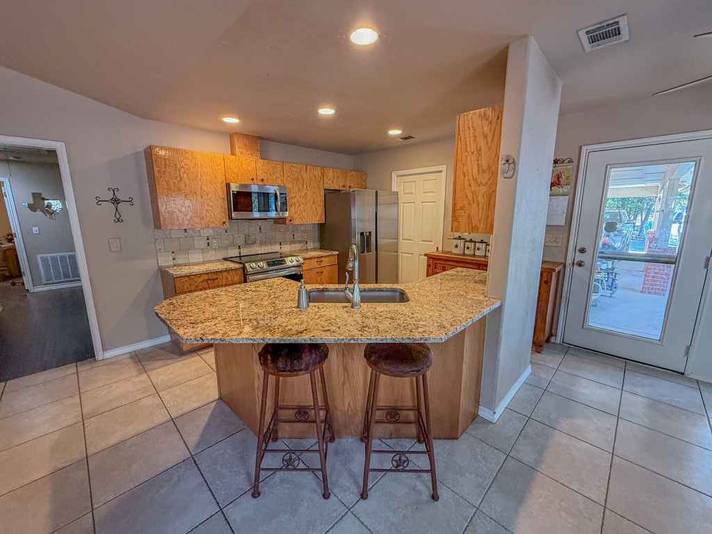 Undisclosed Address Georgetown, TX 78633 - Photo 15 of 37 Kitchen with light stone counters, a breakfast bar, tasteful backsplash, a peninsula, and stainless steel appliances