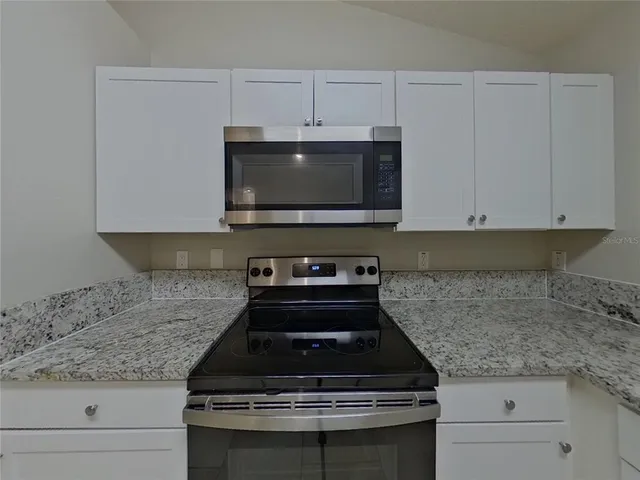 a kitchen with granite countertop a stove and white cabinets