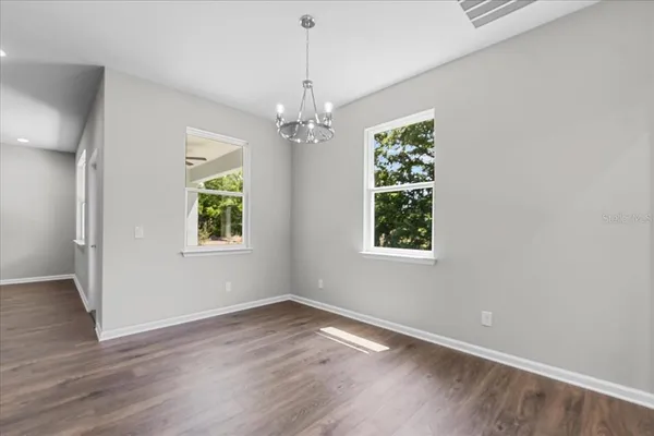 an empty room with wooden floor chandelier and windows
