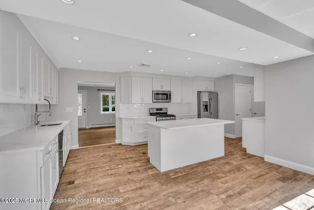 a kitchen with stainless steel appliances granite countertop a stove a refrigerator a sink and white cabinets